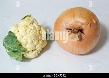 Eine riesige Zwiebel und/oder ein winziger Blumenkohl auf Marmoroberfläche - ein oder beide Gemüse ist ungewöhnlich klein oder unerwartet groß. Zwiebel ist größer als Cauli. Stockfoto