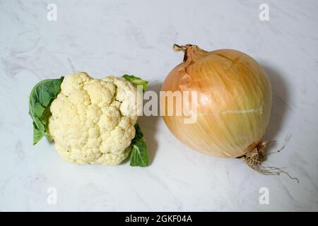 Eine riesige Zwiebel und/oder ein winziger Blumenkohl auf Marmoroberfläche - ein oder beide Gemüse ist ungewöhnlich klein oder unerwartet groß. Zwiebel ist größer als Cauli. Stockfoto