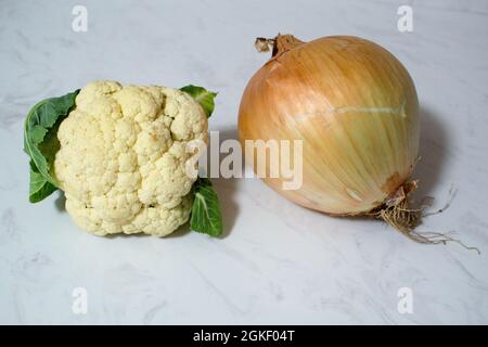 Eine riesige Zwiebel und/oder ein winziger Blumenkohl auf Marmoroberfläche - ein oder beide Gemüse ist ungewöhnlich klein oder unerwartet groß. Zwiebel ist größer als Cauli. Stockfoto