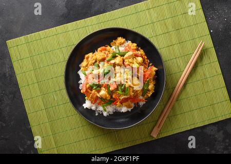 Thailändisches Frühstück Gai Pad Pongali mit Huhn, Eiern, würziger, gelber thai-Paprikapaste, Tomaten, Reis in schwarzer Schüssel im Wok. Nahaufnahme. Panasiatische Küche. Stockfoto