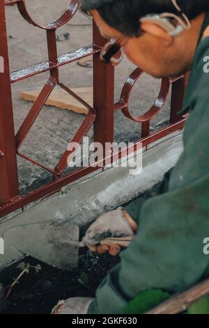 Bautechniker mit Hörgerät, die mit Zementpflaster arbeiten, mischen sich bei Seitenarbeiten im Hinterhof mit Kelle. Zementmörtel Pulver auf Ziegel gelegt. Rea Stockfoto