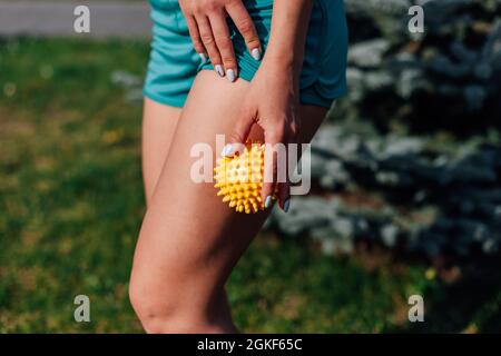 Seitenansicht des schlanken, athletischen Körpers einer jungen Frau, die im Sommer im Park eine Hüftmassage mit einem Stachelball macht Stockfoto