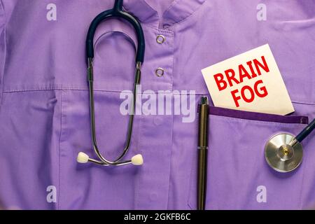 Medizinisches und COVID-19 Pandemisches Coronavirus-Hirnnebel-Symbol. Medizinische Uniform, weiße Karte mit den Worten „Hirnnebel“. Schöner weißer Hintergrund. Speicherplatz kopieren Stockfoto