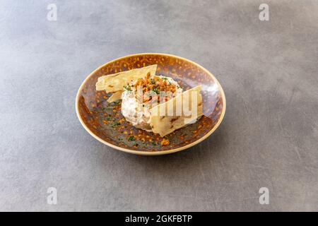 Raffinierte spanische Tapa aus russischem Salat mit gebratenen Garnelen, Schnittlauch und knusprigen Kartoffeln an den Seiten auf einem gerösteten braunen Teller Stockfoto