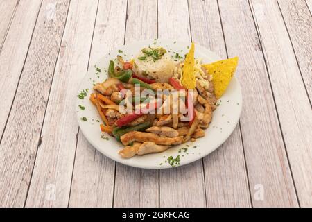 Portion Hähnchenfajitas mit roten und grünen Paprika, Zwiebeln, Nachos und weißem Reis auf einem runden weißen Teller und einem hellen Tisch Stockfoto