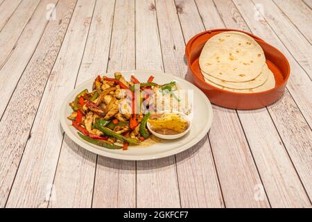 Teller mit Hühnerfajitas mit sautierten roten und grünen Paprika, Zwiebeln, weißem Reis und Käse mit einer Schüssel Weizentortillas, um Tacos zu machen Stockfoto