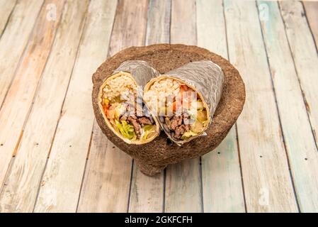 Großer Burrito gefüllt mit Rindfleisch Fajitas, weißem Reis und Bohnen auf einem vulkanischen Stein Molcajete auf einem hölzernen Hintergrund Stockfoto