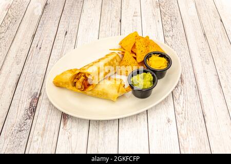 Hühnerfajitas, geschmort mit Cheddar-Käse, Guacamole und Maischips, zum Eintauchen auf einen weißen Teller und hellen Holzhintergrund Stockfoto