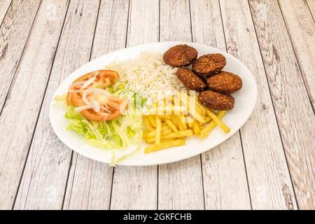 Falafel-Menü mit Kugeln, weißem Reis, pommes frites, Salat und Tomatenscheiben mit weißen Zwiebelstreifen auf hellem Holzhintergrund Stockfoto