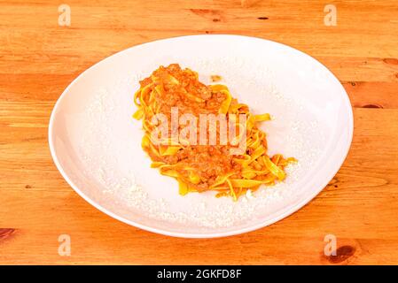 Teller Fettuccine mit italienischer Bolognese-Sauce und viel geriebenem Parmesankäse auf weißem Teller und Holztisch Stockfoto