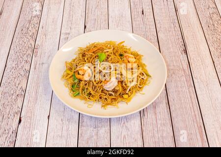 Dünne gebratene chinesische Reisnudeln mit Garnelen und Gemüse im Wok mit Sojasauce auf weißem Teller anbraten Stockfoto