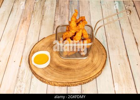 Metallkorb für die Fritteuse voller Hähnchenfinger mit einer Sauce aus einem Stück Holz, wo Sie die Altersringe des Baumes sehen können Stockfoto