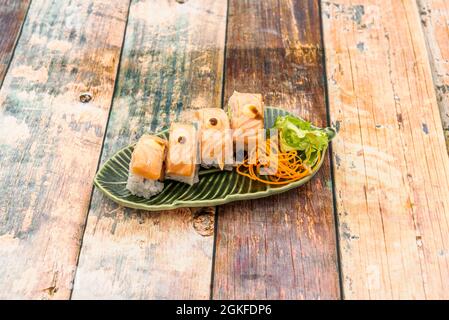 Vier Stücke flambierter Lachs-Nigiri auf einem grünen, blattförmigen Teller Stockfoto