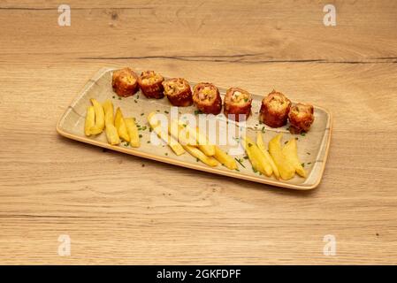 Gehackte andalusische Flamenquin-Tapa, begleitet von pommes frites und mit Schnittlauch auf einem holzfarbenen Teller bestreut Stockfoto