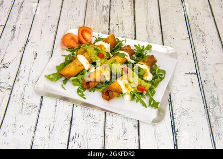 Gebratene gefüllte goldene Maistacos mit Frischkäse und Guacamole auf der Oberseite mit einem Bett aus Rucola-Sprossen auf einem Metalltablett Stockfoto