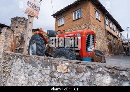 Birgi, Izmir, Türkei - 03.09.2021: Alter roter Traktor, der auf einer Straße geparkt ist, und lokale Steinhäuser in Birgi Stockfoto