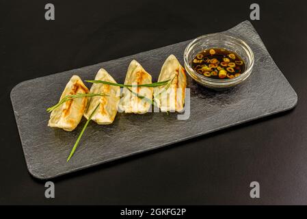 Japanische Knödel, Gyozas, gefüllt mit gedämpftem Fleisch, begleitet von einer Sojaschüssel mit Gemüse auf einem grauen Teller Stockfoto