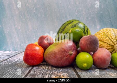 Saisonale Sommerfrüchte auf einem Holztisch. Afrikanische Mango, Limetten, gallenmelone, Wassermelone und reife Pfirsiche Stockfoto
