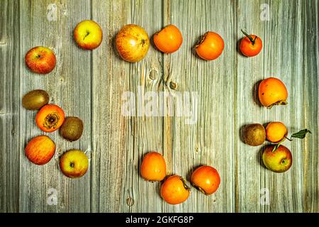 Reife Äpfel, Kiwis, Kaki, Mandarinen und Granatapfel von oben auf einem Holztisch betrachtet Stockfoto