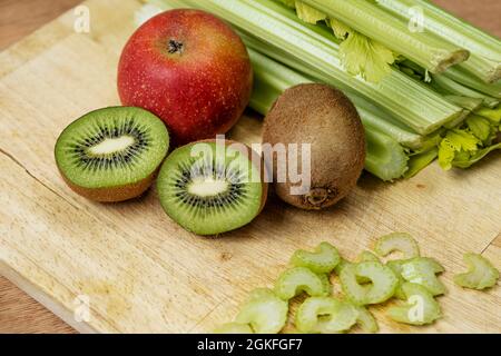 Schneiden von Obst und Gemüse, um köstlichen und natürlichen Detox-Saft mit Kiwi, Apfel und Sellerie auf Holzbrett zu machen Stockfoto