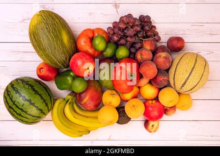 Haufen Früchte auf weißem Tisch. Melonen und Wassermelonen, rote Trauben, reife Bananen, gelbe und rote Pfirsiche, afrikanische Mangos, riesige Tomaten. Stockfoto