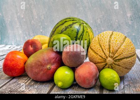 Reife Früchte bereit, an einem Sommertag zu essen. Rote Pfirsiche, grüne Limetten, Melonen und Wassermelonen, afrikanische Mangos auf Holztisch Stockfoto