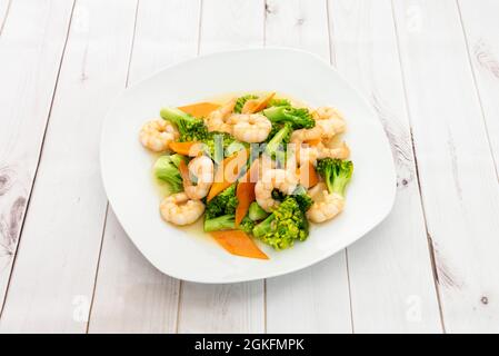 Platte mit gekochten geschälten Garnelen mit Brokkoli al dente und Karottenscheiben auf weißem Teller Stockfoto