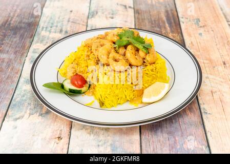 Gebratene geschälte Garnelen auf einer Reisschüssel mit Gemüse und gelber Sauce auf weißem Teller Stockfoto