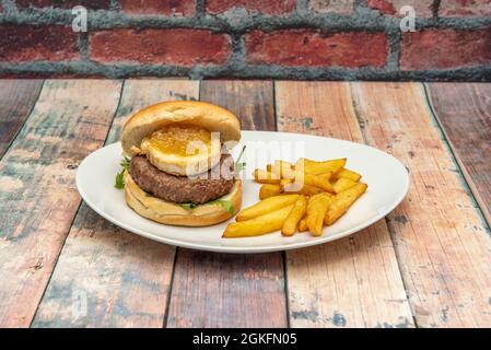 Spektakulärer Rinderburger auf einem Rucola-Bett und auf der Oberseite ein großes Medaillon Ziegenkäse mit Zwiebelmarmelade und hausgemachten Bratkartoffeln auf der ri Stockfoto