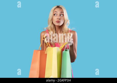 Nachdenkliche Frau, die bunte Einkaufstaschen in der Hand hält und wegschaut Stockfoto