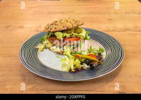 Fantastischer veganer Linsenburger mit Guacamole, Gurken, Tomaten, Salat, Piparra, Schwarze Oliven und Kirschtomaten auf einem schönen Teller Stockfoto