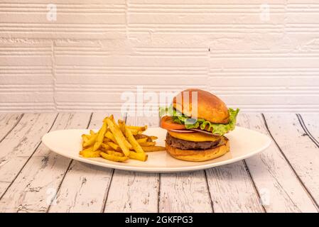 Klassischer Rindfleischburger mit roten Zwiebeln, Tomatenscheiben, Cheddar-Käse und Eisbergsalat auf einem weißen Tablett und einer Seite Pommes frites Stockfoto