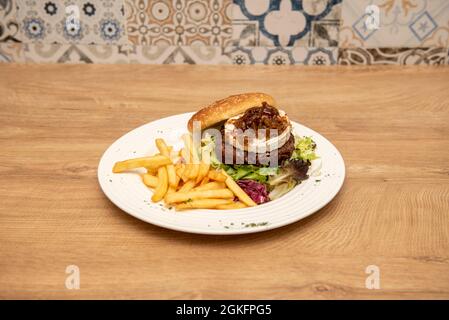 Rinderburger mit Ziegenkäse und karamellisierten Zwiebeln, verschiedenen Salatsprossen und Pommes frites Stockfoto