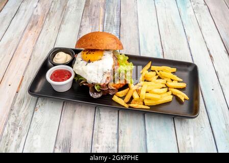 Köstlicher Rindfleischburger mit Salatsprossen, Speck, Tomatenscheiben, Spiegelei mit Trüffelspan, Mayonnaise und Ketchup-Saucen, garniert mit Französisch Stockfoto