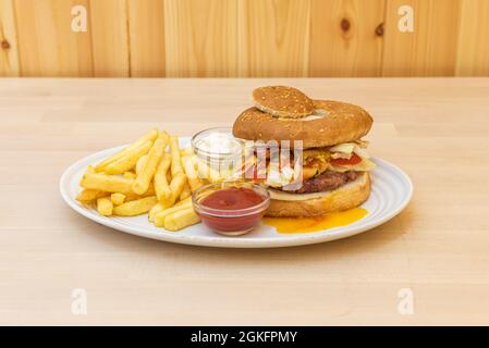 Spezieller Hamburger mit frittiertem Eigelb auf Salat und Fleisch, zwei Kugeln mit Mayonnaise und Ketchup-Sauce und einer Seite Pommes frites Stockfoto