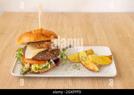 Rindfleisch-Burger mit Käse und karamellisierten Zwiebeln und einigen Kartoffelkeilen garnieren auf einem Eichenholztisch Stockfoto