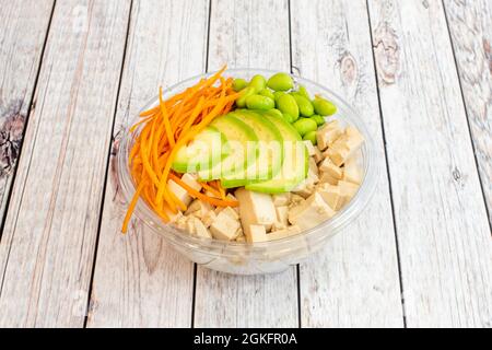 Vegane Schüssel mit hawaiiianischen Poke mit Scheiben mexikanischer Avocado, japanischen Edamame-Bohnen, geriebenen Karotten und vielen Tofu-Tacos auf einem transparenten Take Away Stockfoto