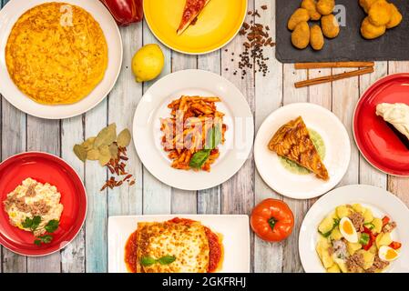 Blick von oben auf typische mediterrane Gerichte aus Spanien und Italien. Apfelkuchen, Salat-Tapas, gekochte Kartoffeln, Kroketten, Lasagne, Usw. Stockfoto