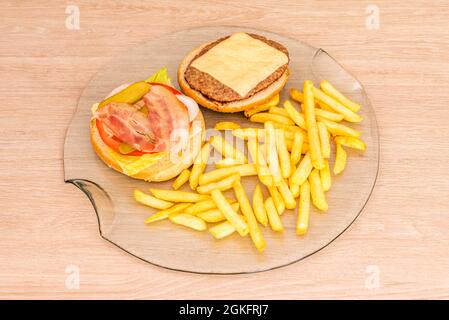 Der klassische Hamburger wird offen auf einer transparenten Glasplatte mit Pommes frites präsentiert Stockfoto