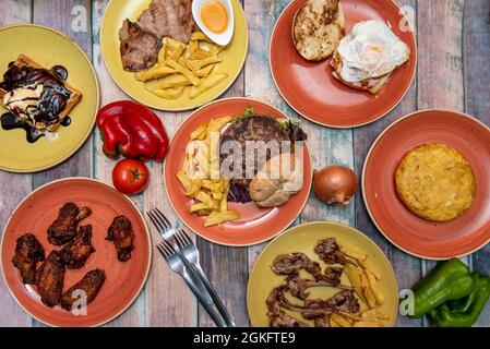 Eine Reihe von Gerichten der traditionellen spanischen Küche. Lammkoteletts, Kartoffelomelett, Rinderfilet mit hausgemachten Pommes frites, Waffel mit Vanilleeis, xl-Hamburger Stockfoto