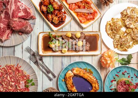 Bild von oben mit raffinierten Gerichten der spanischen Gastronomie. Gegrillter Oktopus mit violetter Mayonnaise, Steak mit runden Kartoffeln, gebratenes Artischockenherz Stockfoto