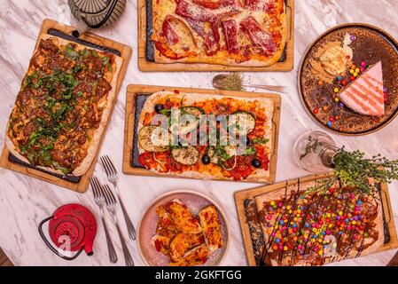 Süße und herzhafte rechteckige Pizzas. Pizza mit serrano-Schinken und Käse, mit schwarzen Oliven und Zucchini, mit Lacasitos und Schokolade Stockfoto