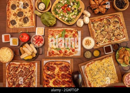 Rechteckige Pizzas mit Käse, Pilzen, verschiedenen Kirschtomaten, frischen Rucola, rohen Artischocken, Salat mit Huhn, Hähnchenflügel, tequeños Stockfoto