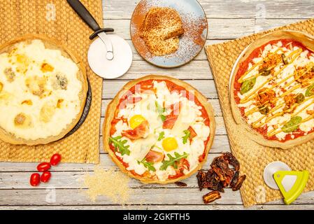 Pizzas mit viel Mozzarella-Käse von oben gesehen mit Firots-Eiern und Schinken, mit Avocado und Schweinefleisch, Kirschtomaten und getrockneten Tomaten, piz Stockfoto