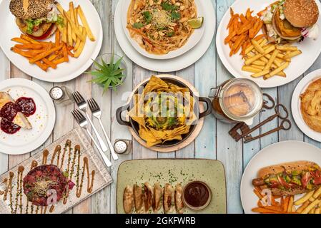 Ansicht von oben von Lebensmitteln. Nachos mit Guacamole und Jalapenos, Gyozas, Dim Sum, Hamburguesa mit Kartoffeln, roter Thunfisch-Tartare, Tagliatelle mit Nüssen, Schlüsseln Stockfoto