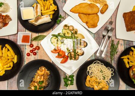 Mediterrane Gerichte und Burritos, Hühnerschnitzel, Garnelenreis, Kirschtomaten, Pommes Frites, Gabeln, wilder Spargel, gegrilltes Gemüse Stockfoto