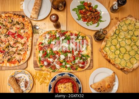 Italienische Gerichte mit Olivenöl, getrockneten Tomaten, Zucchini-Pizza, Pizza mit Burrata und serrano-Schinken, Pasta und Calzone Stockfoto