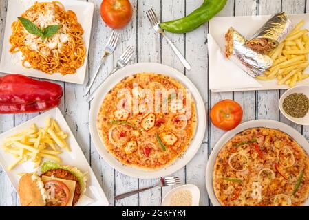 Bild von oben: Pizzakebab mit Zwiebel und Hühnerfleisch, Spaghetti mit Käse, Hamburger mit Pommes, Lahmacun in Aluminiumfolie gerollt und Gabeln Stockfoto