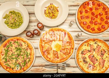 Blick von oben auf italienische Pastagerichte und typische Pizzas mit Guanciale und Pepperoni auf dem Holztisch Stockfoto