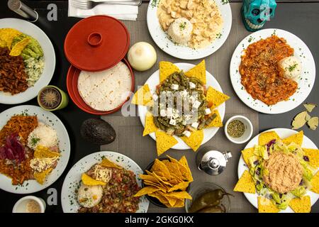 Bild von oben mit mexikanischen Gerichten. Nachos mit Nopales, Chicken Tinga, Chili con Carne, ganze jalapeños, Maiskuchen, Lila Zwiebel, Kürbisblüte Stockfoto